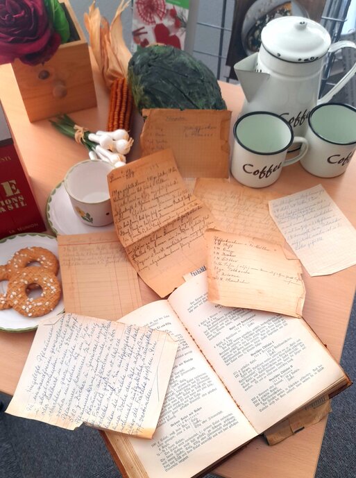 Auf einem Tisch stehen eine Kaffeekanne und Tassen. Ein Teller mit Keksen. Davor liegen alte Bl�tter mit Kochrezepten und ein sehr altes Kochbuch.